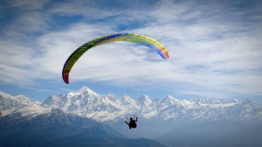 Silhouette man paragliding by snow covered mountains against sky