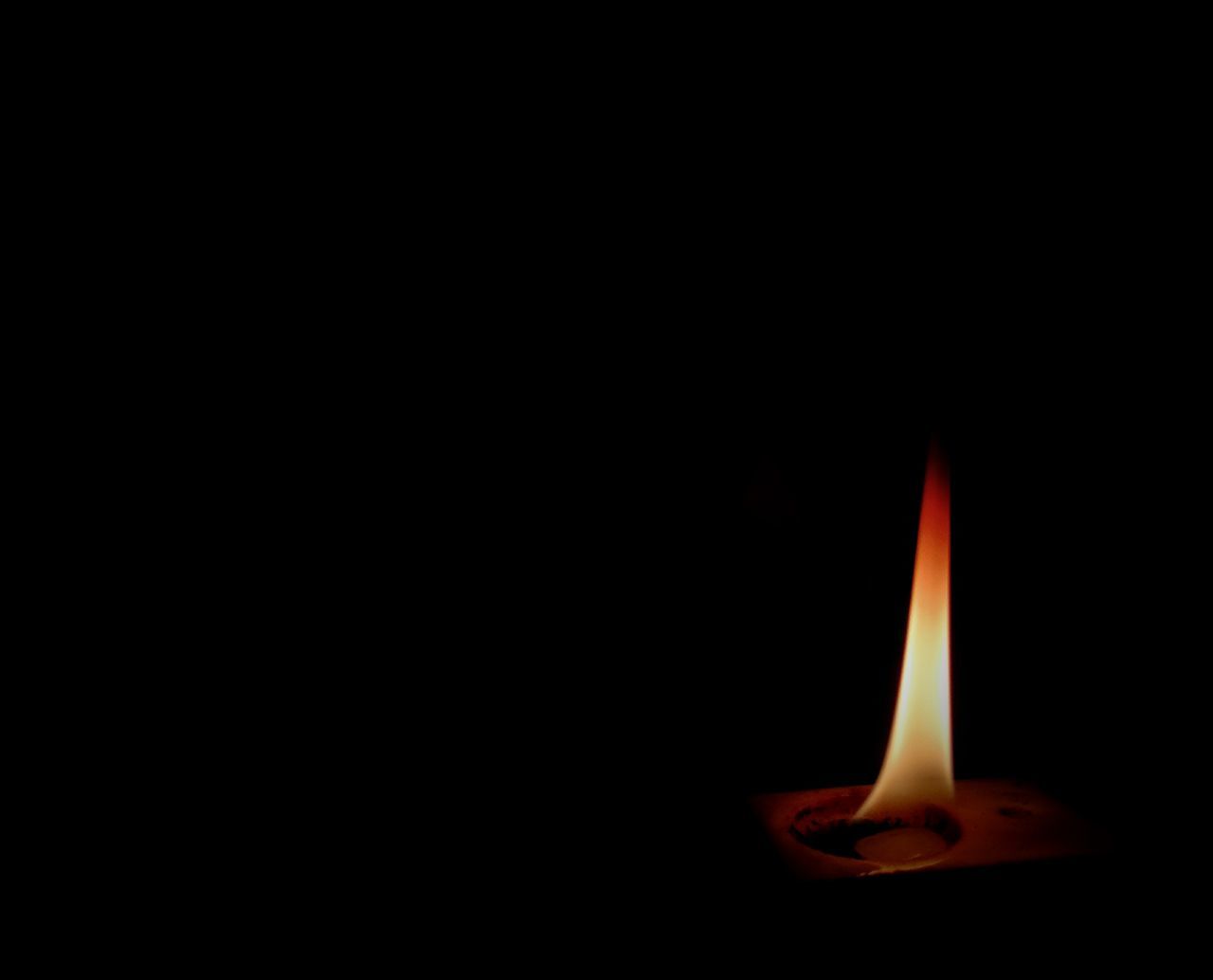 CLOSE-UP OF BURNING CANDLE IN DARKROOM