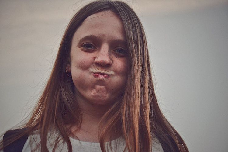 Portrait of smiling young woman making a face against sky