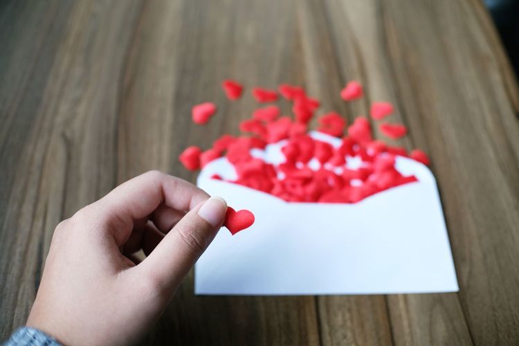 Cropped hand of woman holding heart shape over envelop