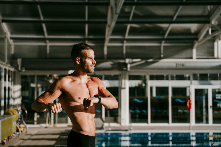 Shirtless male swimmer doing warm up exercise at poolside