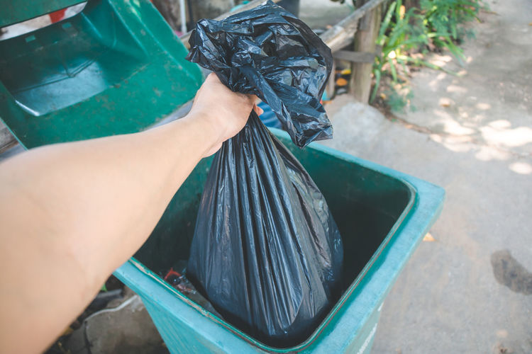 Cropped hand of woman putting plastic bag in dustbin