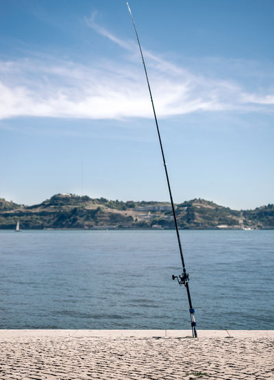 Fishing rod by sea against sky