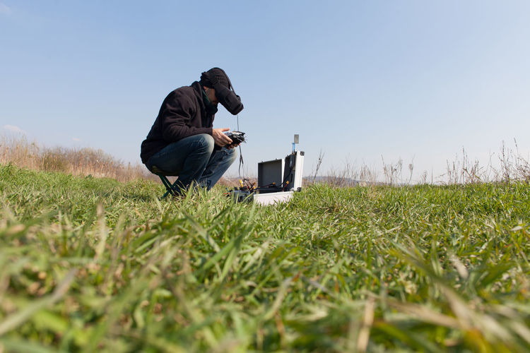 Man wearing virtual reality headset using remote control on grassy field against clear sky