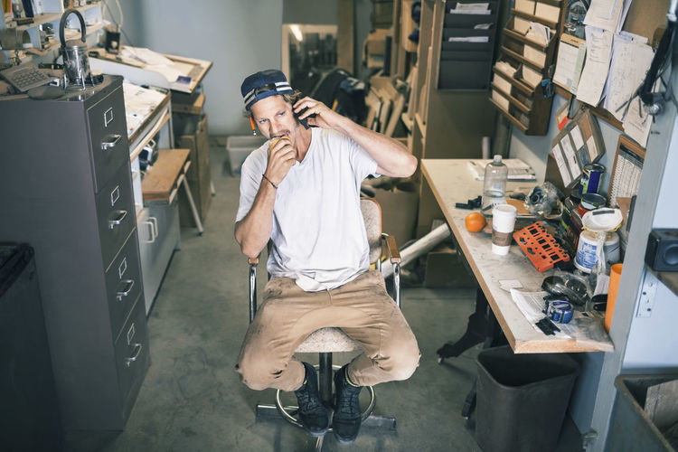 High angle view of carpenter using mobile phone while sitting in workshop