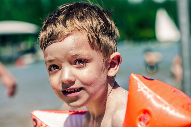 Close-up portrait of shirtless wet boy with water wings on shore