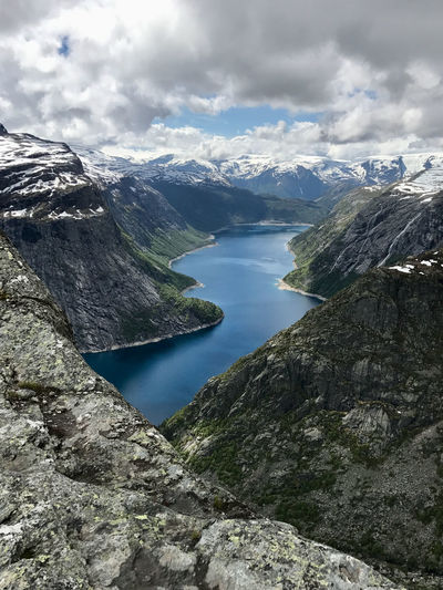 Scenic view of lake, waterfalls, and snow capped mountains against sky in norway near trolltunga