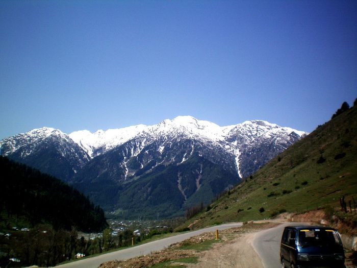 Road amidst snowcapped mountains against clear sky during winter