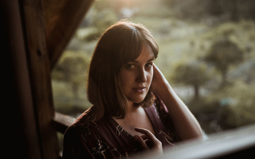 Portrait of young woman on ledge of wooden cabin at sunset