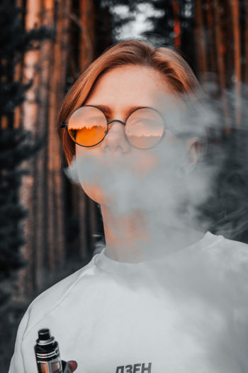 Close-up portrait of young woman exhaling smoke while standing in forest