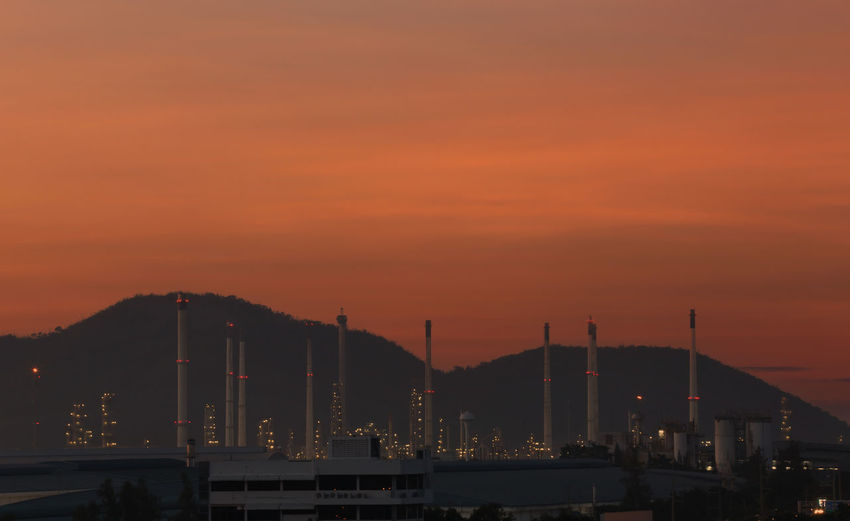 Illuminated factory against orange sky