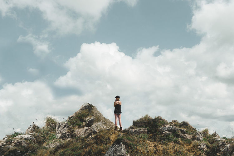 Rear view of woman standing on mountain peak against cloudy sky