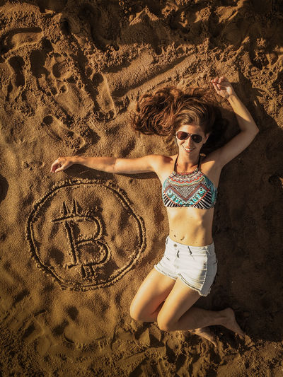 Full length of woman lying by bitcoin symbol at beach