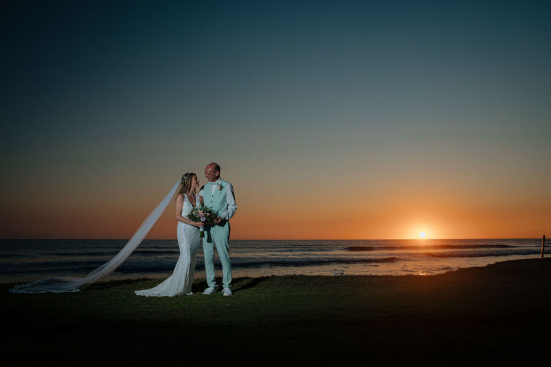 Marriage on beach against sky during sunset