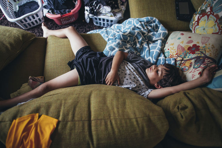 Overhead view of boy sleeping on messy sofa at home