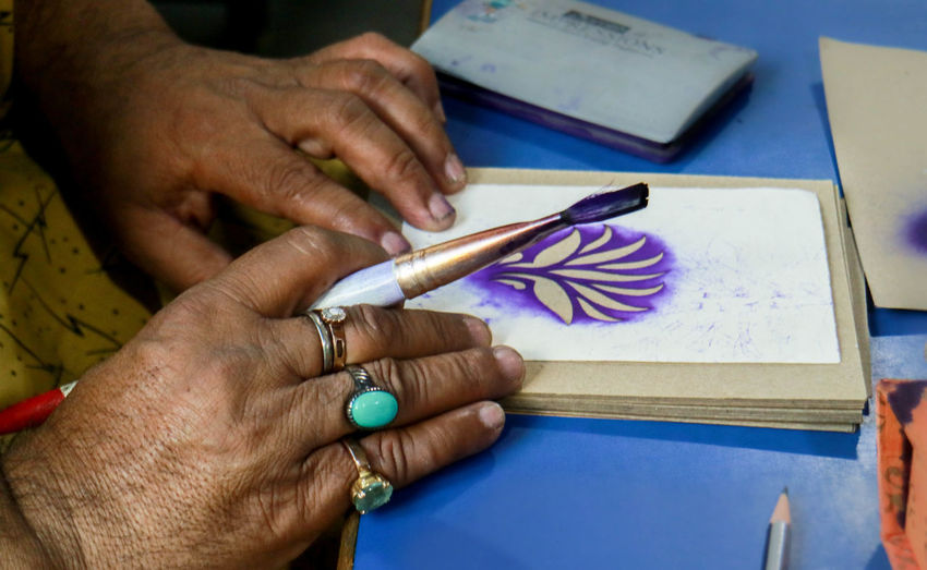 Cropped hands of artist with paintbrush making floral pattern on paper