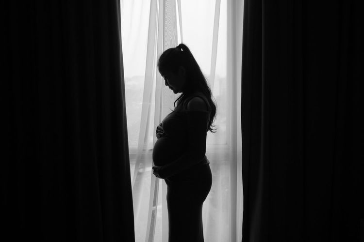Side view of pregnant woman standing against curtain 