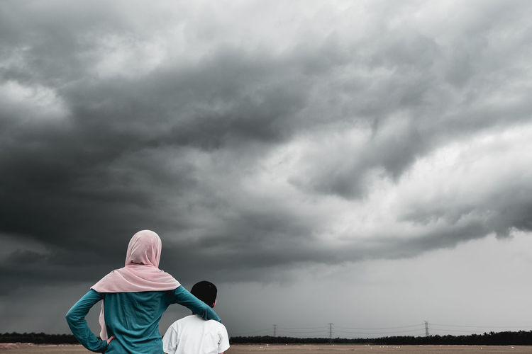Rear view of siblings looking at stormy clouds
