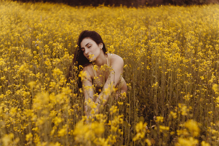 High angle view of young woman with eyes closed in bikini sitting amidst flowers on field
