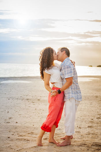 Couple kissing while standing at beach against sky