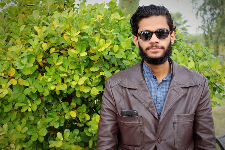 Portrait of young man wearing sunglasses while standing against plants