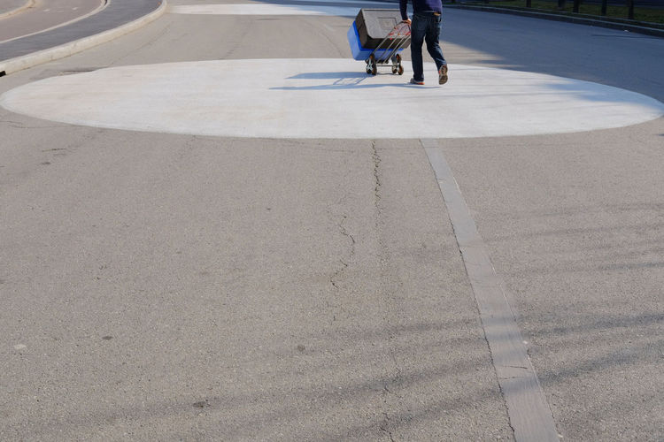 Low section of man pushing forklift with containers while walking on road