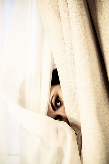 Portrait of woman hiding behind curtain