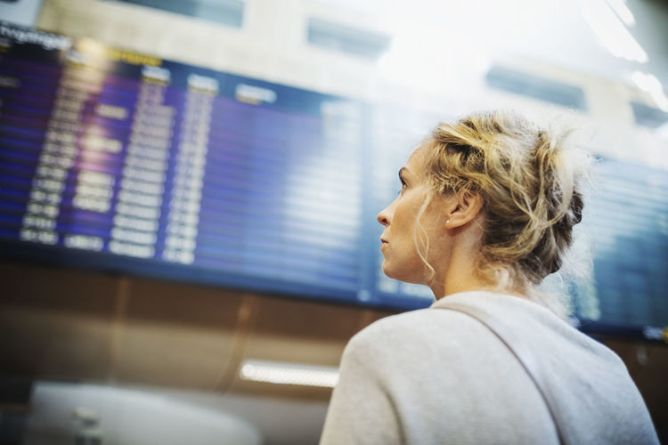 Rear view of businesswoman looking at arrival departure board in airport