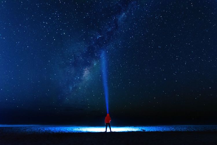 Rear view of person with illuminated flashlight standing against star field at night