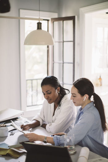 Side view of architect discussing with coworker while working at table in home office