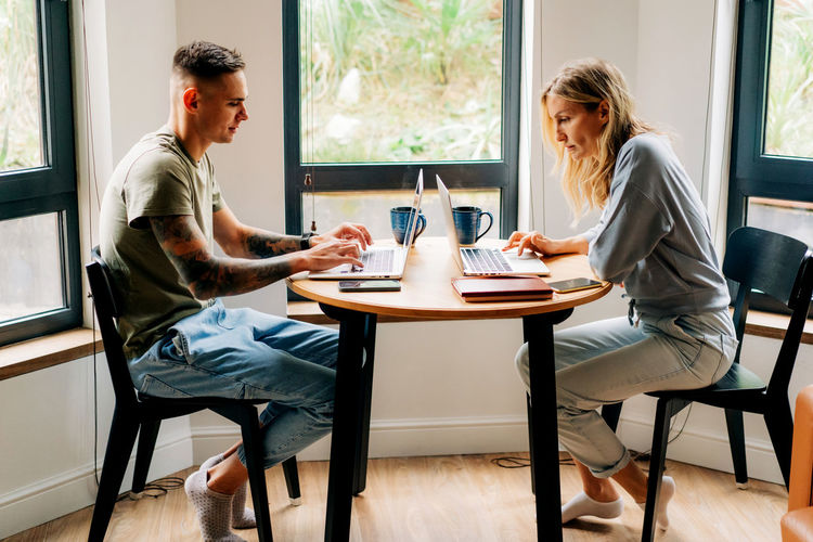Busy young man and woman work online on laptops at home at the table in the living room