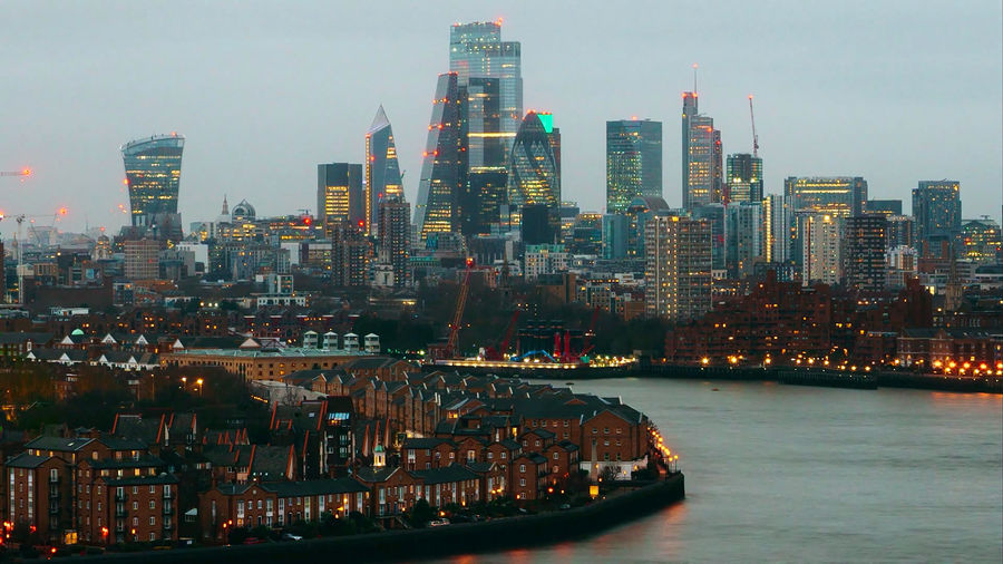 Illuminated buildings by river against sky in city