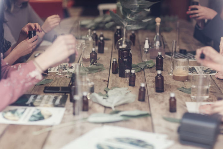 Cropped hands of multi-ethnic female colleagues preparing perfumes at table in workshop seen from window