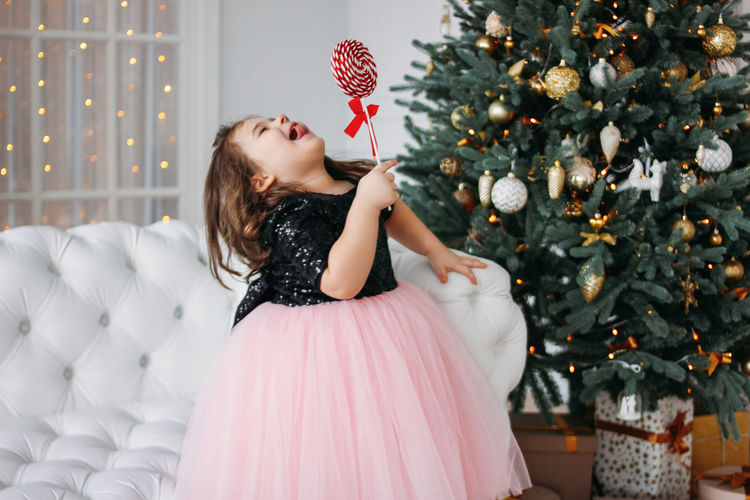 Happy girl with candy standing against christmas tree