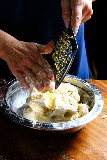 Unrecognizable female removing fresh lemon peel from metal grater over bowl with pastry dough in kitchen