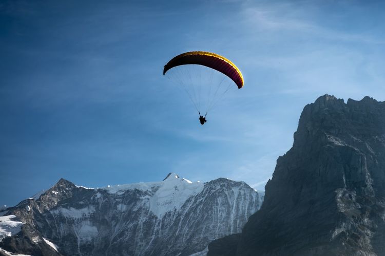Low angle view of person paragliding over mountains against sky