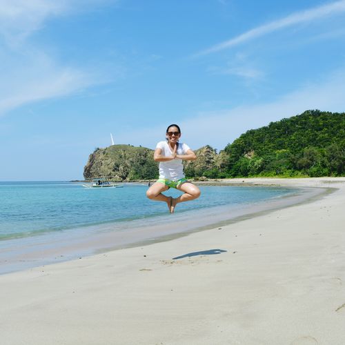 Full length of woman levitating at beach against sky