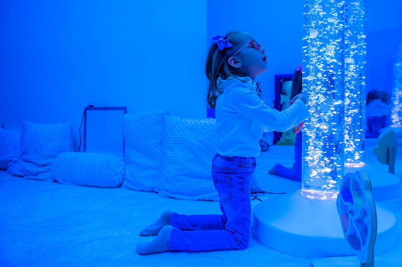 Child in sensory room, snoezelen, interacting with colored lights bubble tube lamp during therapy.