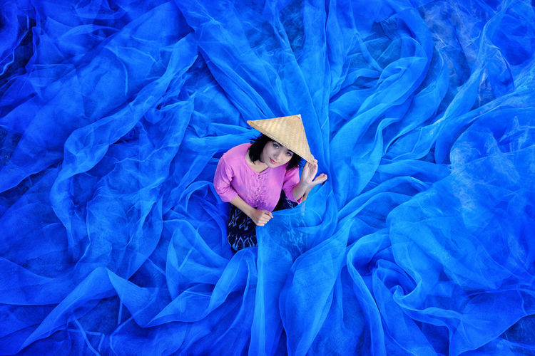 Young woman wearing asian style conical hat holding blue tulle netting
