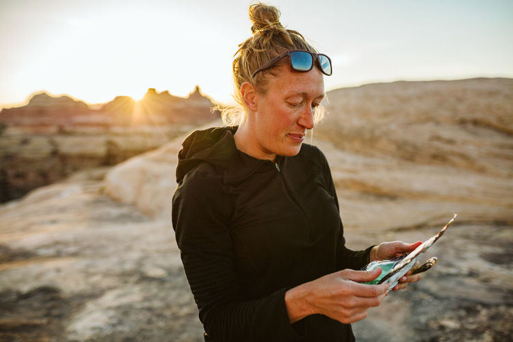Woman in black reads ingredients off freeze dried dinner in desert