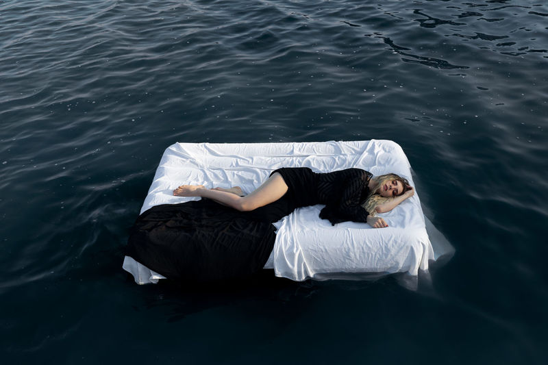 High angle view of young woman sleeping on bed floating in lake