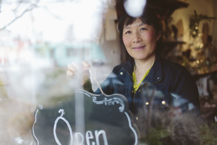 Female owner hanging open sign on window of garden center seen through glass