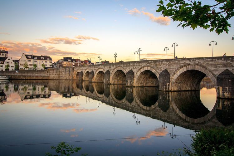 Bridge over river against sky at sunset
