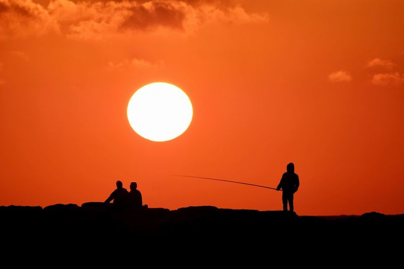 Silhouette men on pier against orange sky