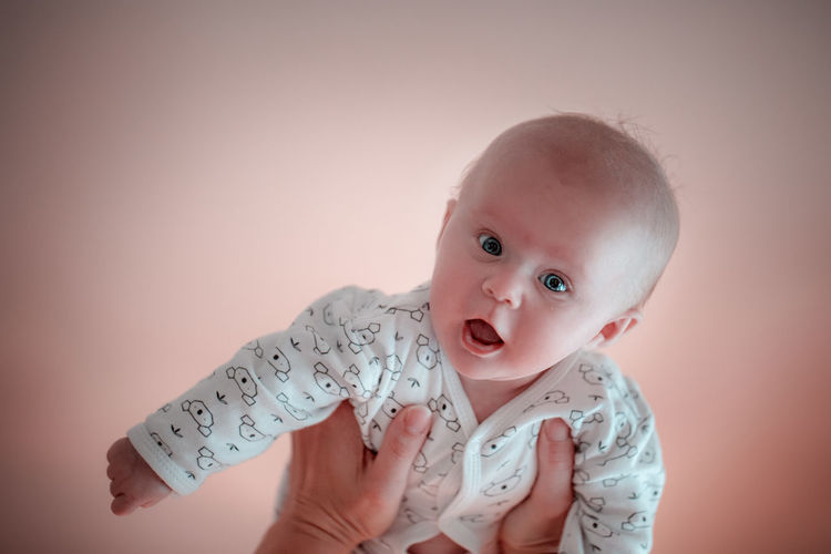 Cropped hands holding baby girl against colored background