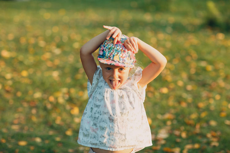 Portrait of cute girl with arms raised making face while standing on grass