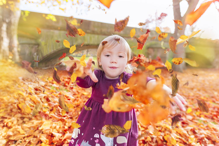 Girl throwing autumn leaves on field