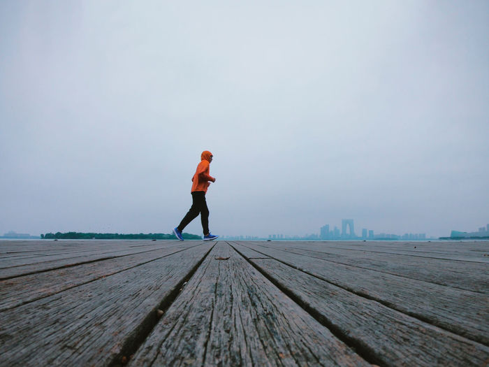 Side view of man jogging on boardwalk against sky