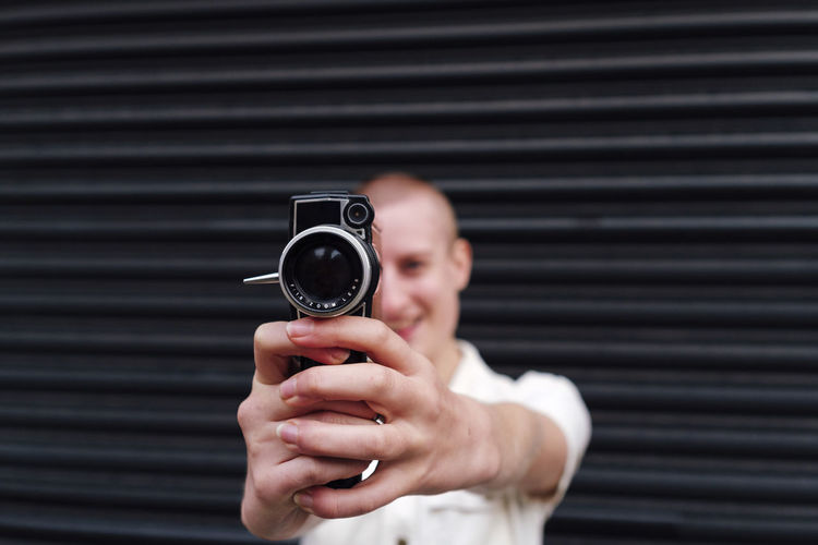 Non-binary person holding video camera in front of shutter