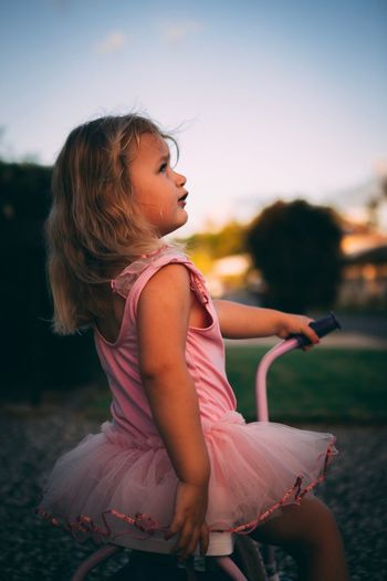 Toddler girl on bike looking at sunset
